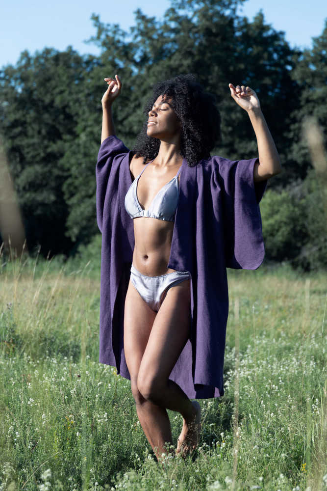 Eine junge schwarze Frau tanzt in einer Wiese in Schweden. Sie trägt handgemachte Lingerie aus Seide und einen nachhaltigen Kimono.